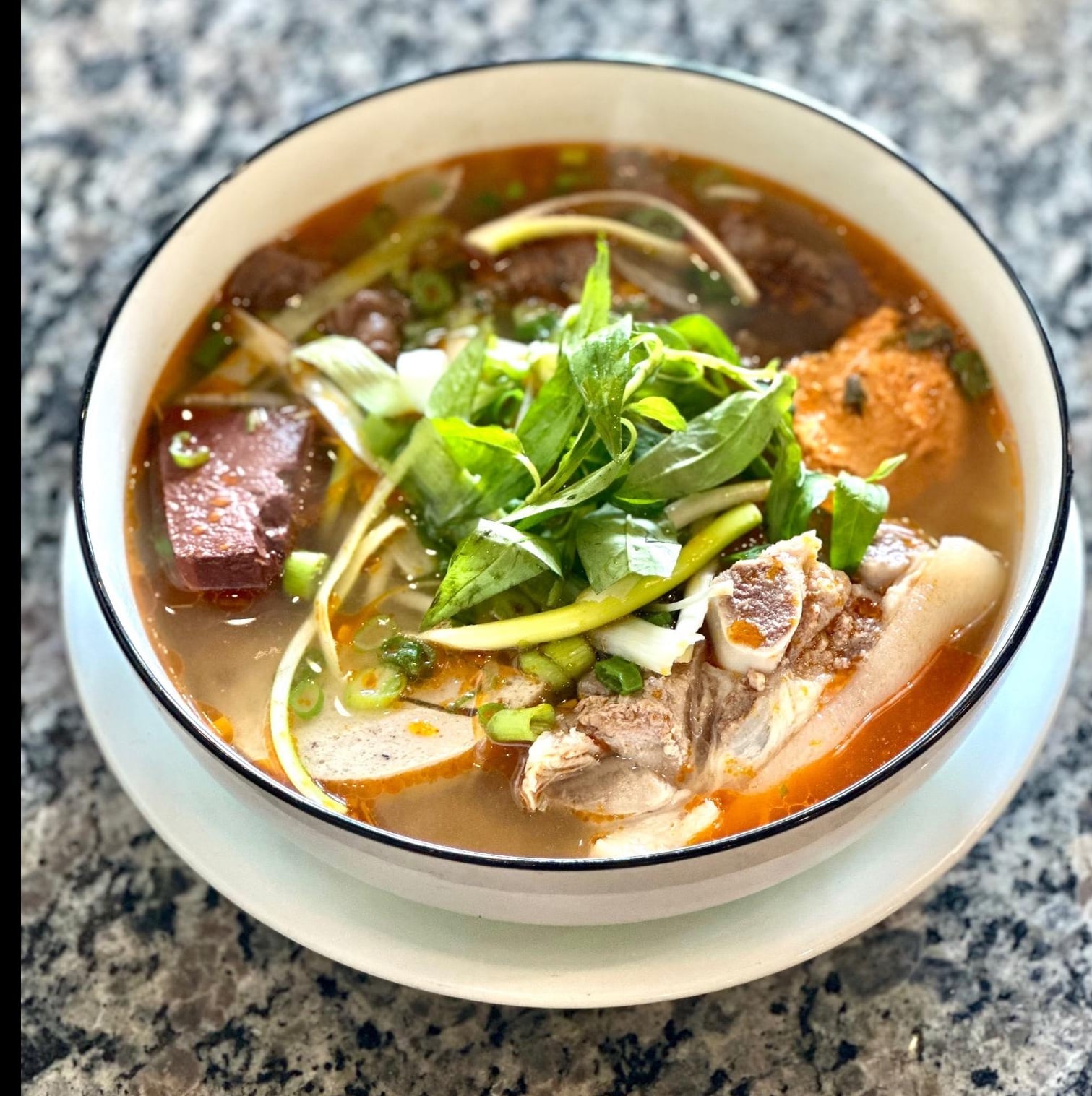 Bowl of Special Hue beef noodle soup with fresh herbs